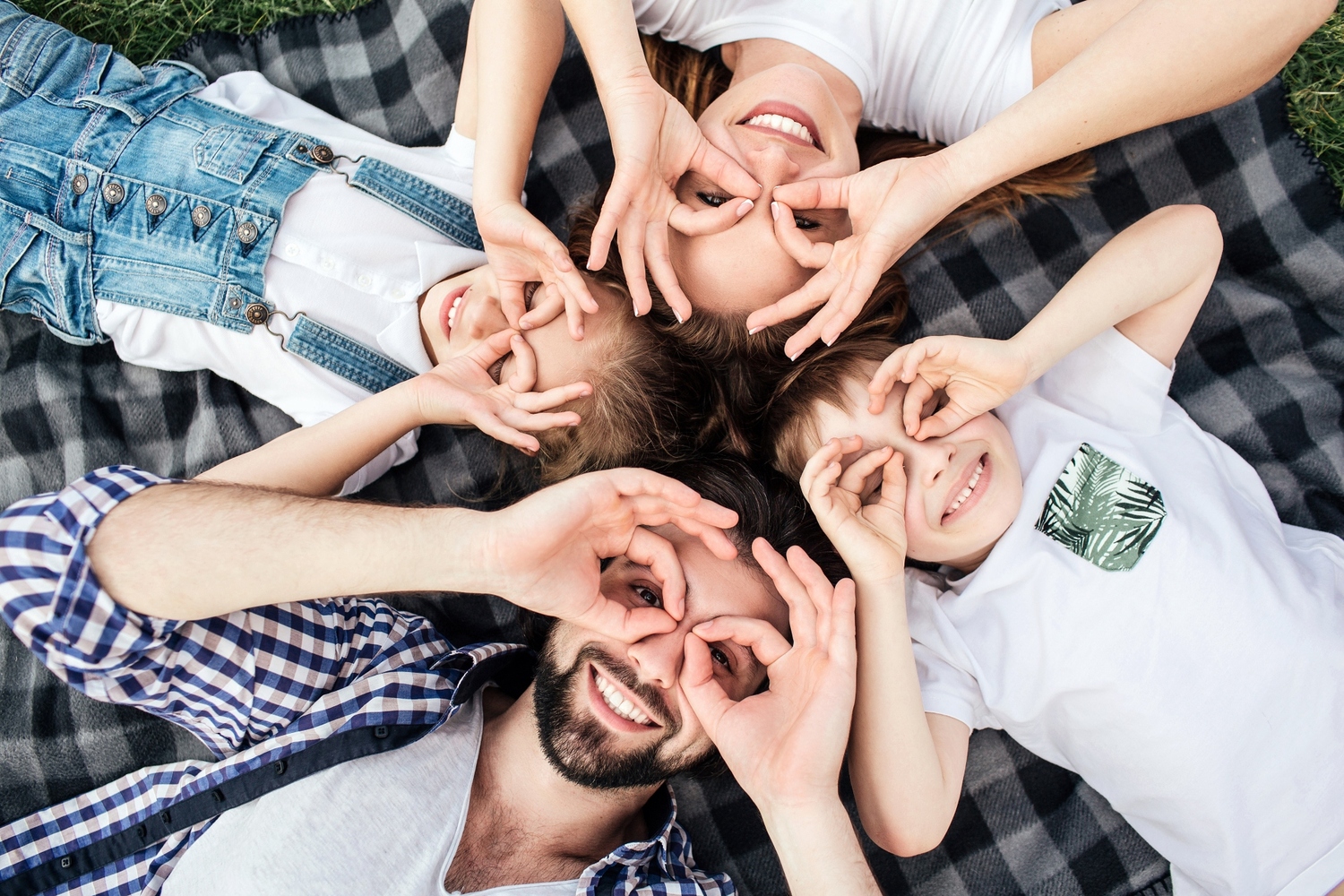Funny picture of family doing funny rounds with their fingers on eyes. They are playing. All of them are lying on blanket and smiling. They look happy